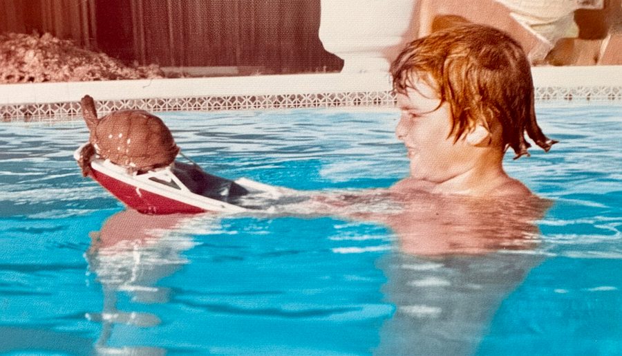 Steve Barnes as a young boy in a swimming pool with a toy turtle on a boat, 1973